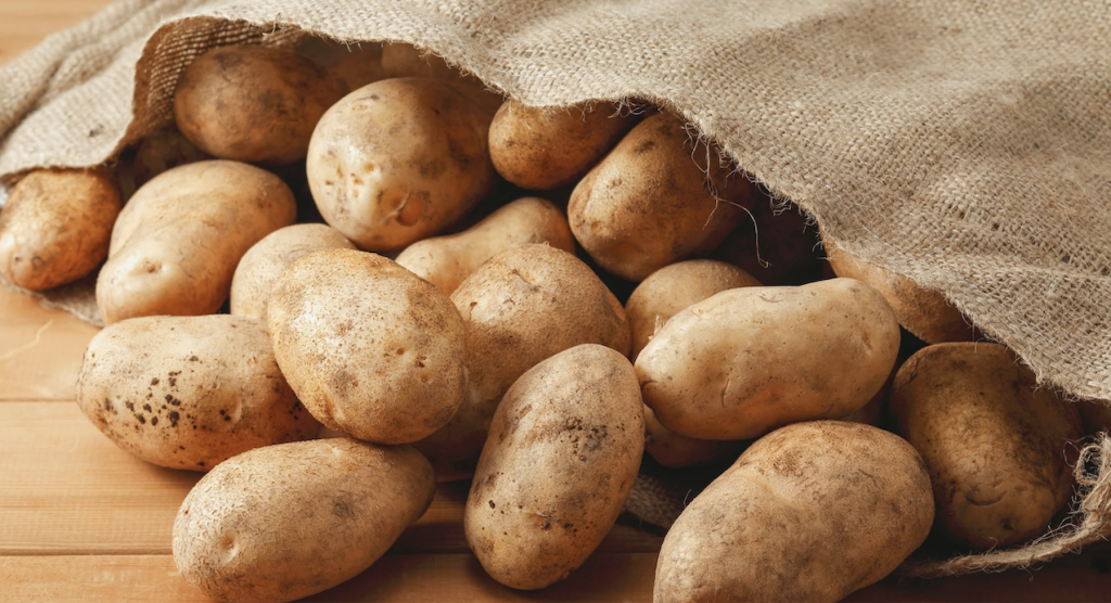 Fresh, whole potatoes spilling out of a burlap bag on a wooden table.
